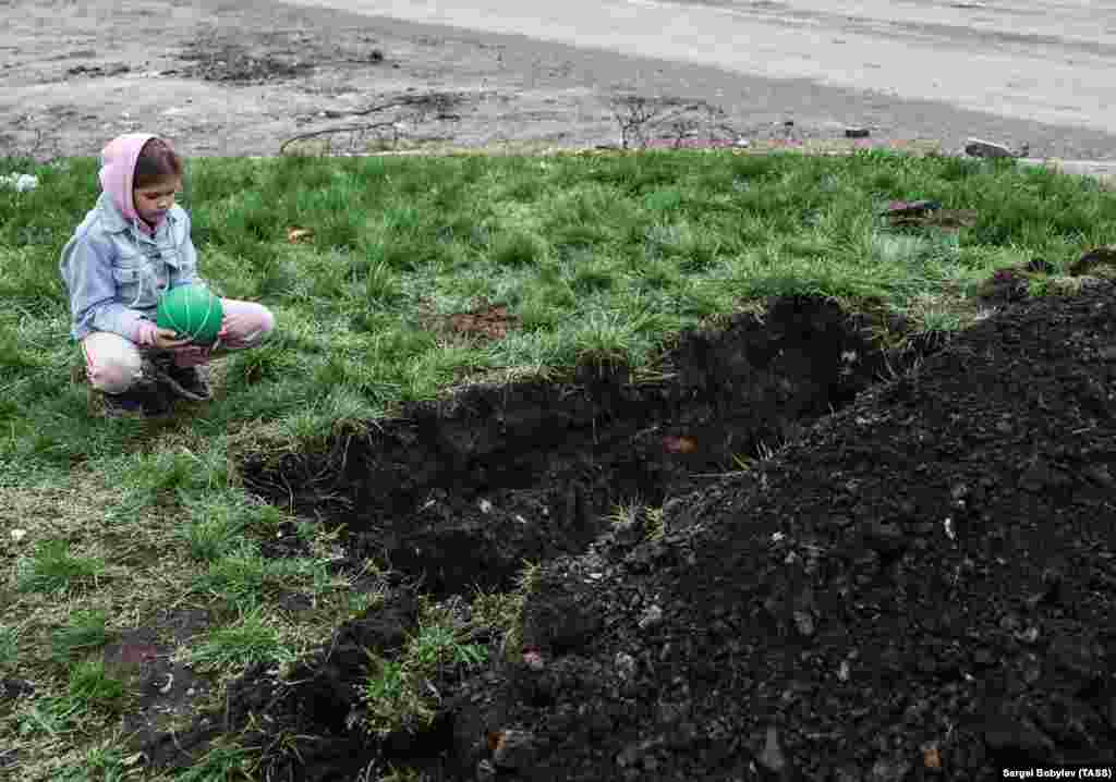 A girl next to a grave dug alongside a road during the siege of Mariupol in April. Some of those buried in Mariupol’s parks and green spaces have also been reburied in the Starokrymske cemetery. 